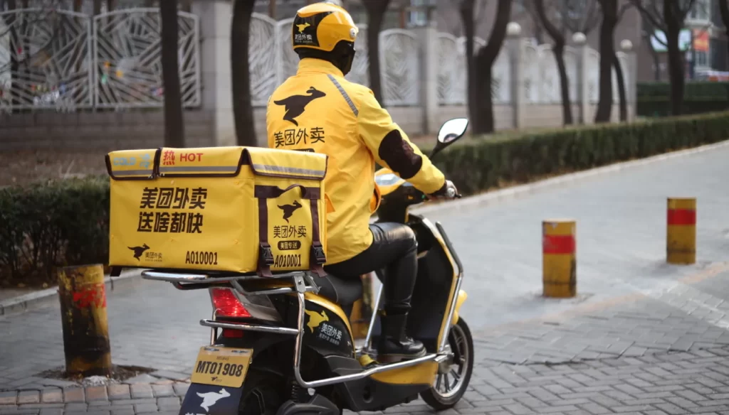 Smartphone screen displaying the Meituan app interface with food delivery options, hotel bookings, and travel services. Highlights Meituan's diverse offerings and its integration with WeChat through the Meituan mini-program.